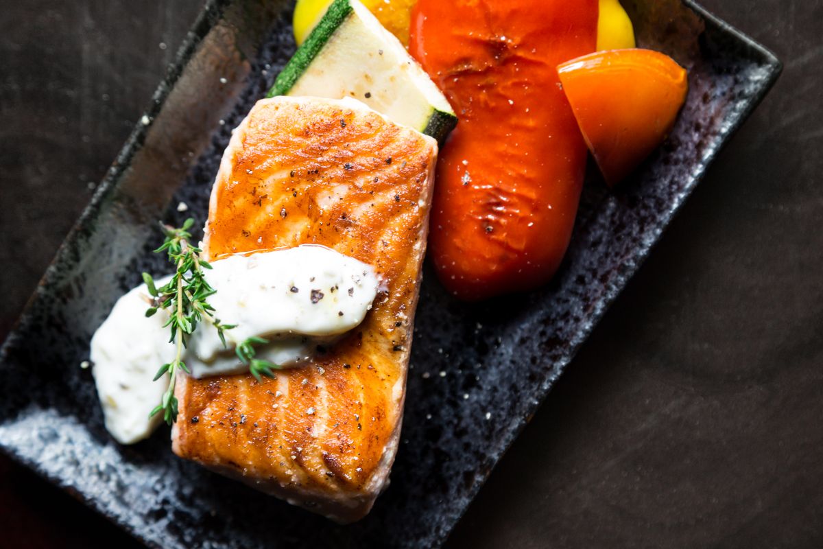 Seared salmon with roasted vegetables on a dark plate